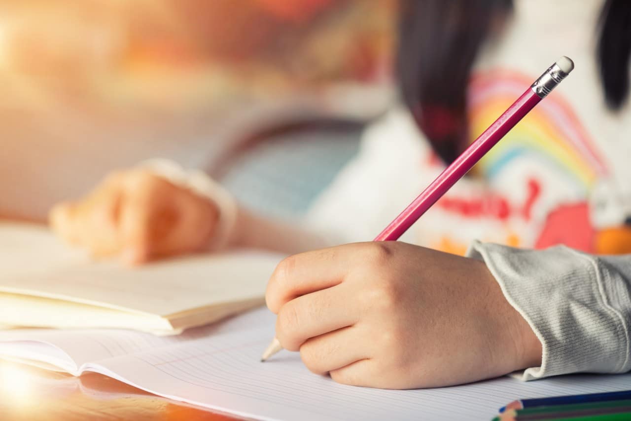 Home Education Child writing with a pencil in a notebook at a desk.