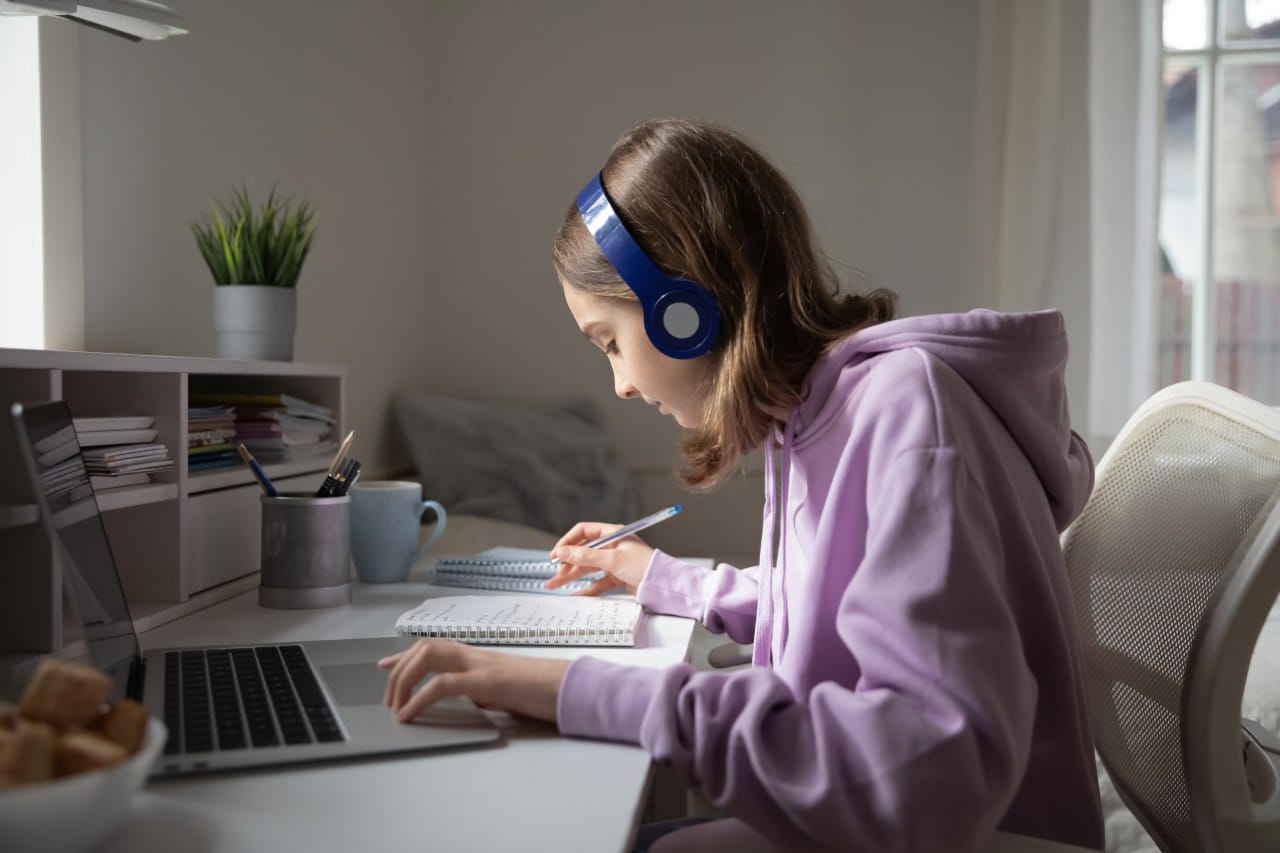 Learn Anytime, at a Pace That Feels Right Girl in headphones studying at a desk with a laptop and notebook.
