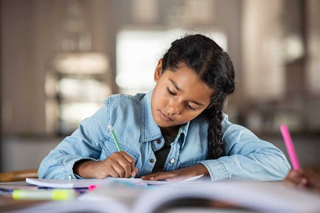 Safeguarding Young girl sitting at a table, writing in a notebook with a pencil.