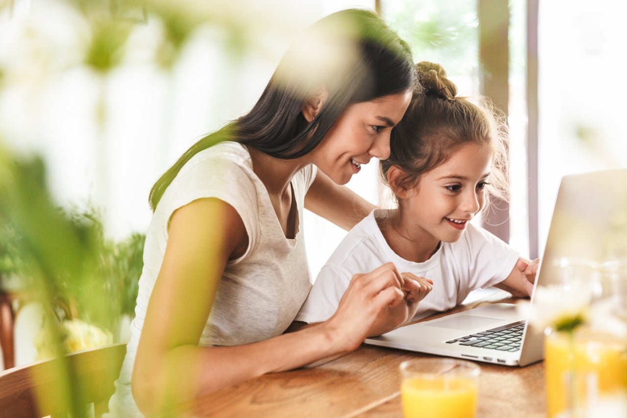 Woman and young girl smiling while using a laptop together at a table.
